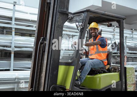 Portrait of a worker operator in a metal warehouse wearing personal protective gear sits in a forklift to transport and load heavy materials. Stock Photo