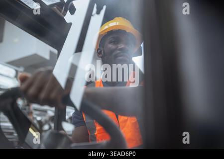 Portrait of a worker operator in a metal warehouse wearing personal protective gear sits in a forklift to transport and load heavy materials. Stock Photo