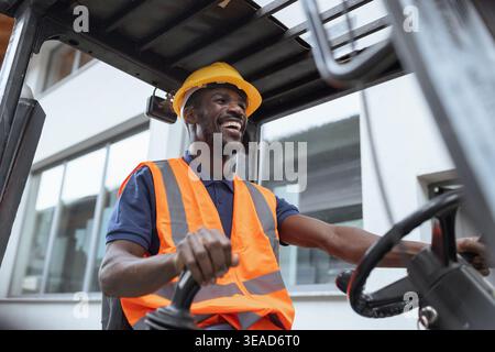 Portrait of a worker operator in a metal warehouse wearing personal protective gear sits in a forklift to transport and load heavy materials. Stock Photo