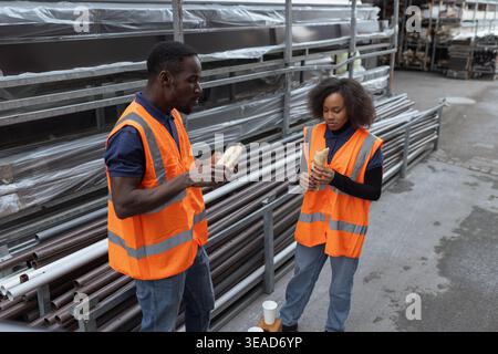 Two colleagues, warehouse workers having a lunch break, enjoying sandwiches and relaxed chat with a smile and coffee after a hard work. Stock Photo