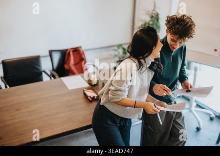 Two students collaborating and smiling over papers in a casual meeting room Stock Photo