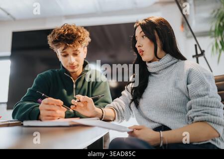 Two students collaborating on homework and studying together at a modern classroom table Stock Photo