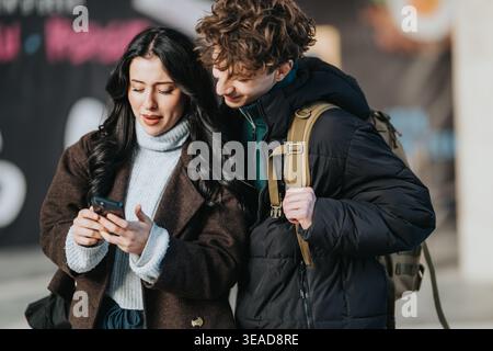 High school friends checking a smartphone together on a city street in winter coats Stock Photo