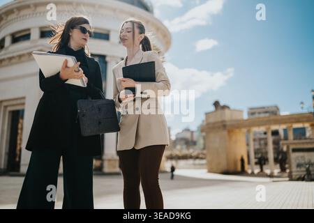Two professional women having a business conversation outside a classical city building on a sunny day Stock Photo