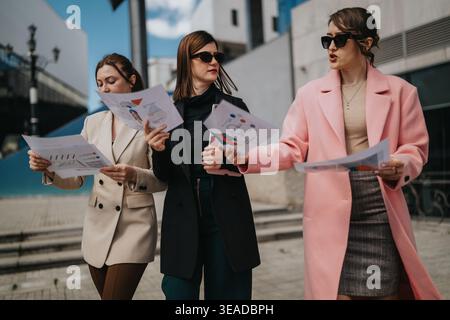 Three businesswomen discussing reports and charts outdoors while walking in an urban area Stock Photo