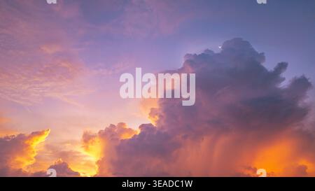 A vivid and dynamic sky captures towering storm clouds illuminated by the warm hues of a setting sun, creating a striking contrast between light and s Stock Photo