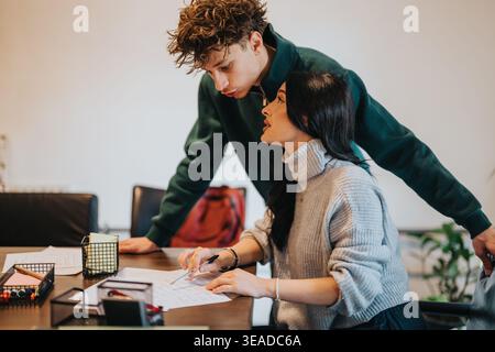 Two students studying together at a table collaborating on paperwork and homework Stock Photo