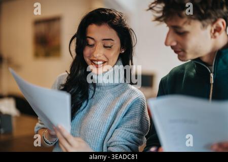 Two students smiling while studying together and reviewing papers in a casual indoor setting Stock Photo