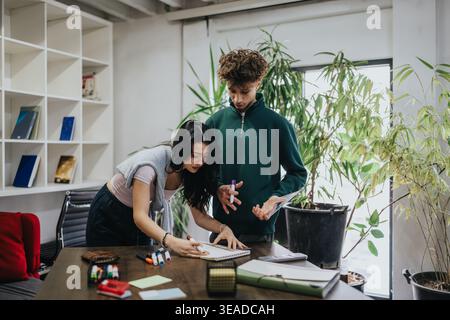 Two students collaborating on a project at a table in a modern study workspace Stock Photo
