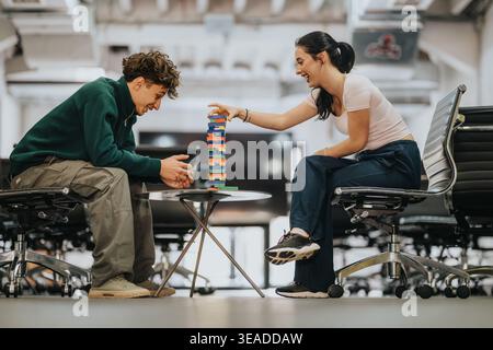 Two students playing a tabletop block game together in a modern co‑working or study space Stock Photo