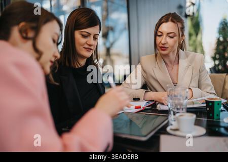 Three female colleagues discussing work over coffee during a business meeting at a cafe Stock Photo