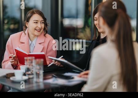 Business colleagues meeting at a cafe discussing notes and plans with smiles and notebooks Stock Photo