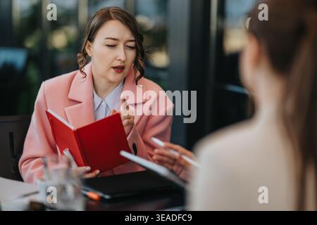 Businesswoman discussing notes with colleague during a professional meeting over a red notebook Stock Photo