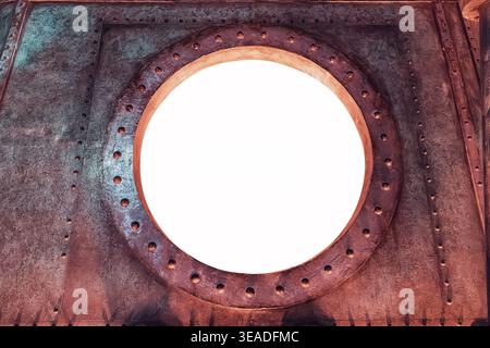 Steampunk style porthole frame on a textured metal wall with rivets, providing a circular white isolated copy space Stock Photo