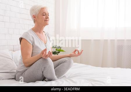 Senior woman doing yoga on bed at home Stock Photo