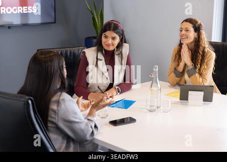 Diverse female coworkers meeting in modern conference room, taking notes on blue folder and tablet Stock Photo