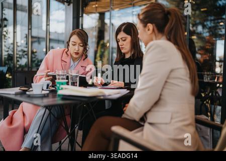 Three businesswomen having an outdoor business meeting and reviewing documents at a cafe table Stock Photo