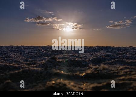 Shot at water level, choppy waves fill the foreground while the sun breaks through scattered clouds on the horizon, casting soft rays. Stock Photo