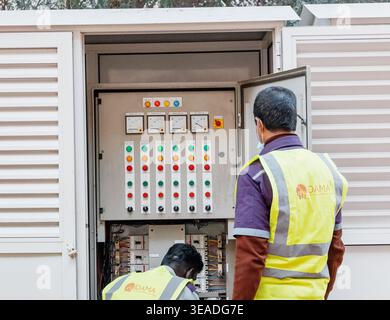 14 January 2026, Dubai, UAE: Electrical technicians in safety vests inspecting and maintaining outdoor power control panel, troubleshooting meters and Stock Photo