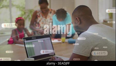 Typing man in gray T-shirt using laptop at home dining table with notification overlays, copy space Stock Photo