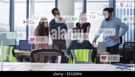 Collaborating team of 5 in office wear reviewing plans on laptops at open office, overlays, vests Stock Photo