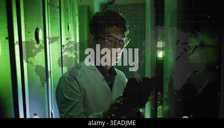 Inspecting Korean man in white lab coat holding tablet beside server racks, holographic map overlay Stock Photo