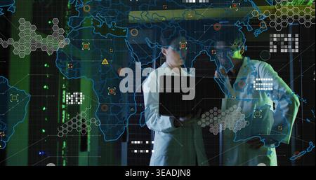 Holding open laptop, two researchers in lab coats examining HUD map over server racks with LEDs Stock Photo