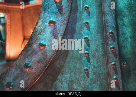 Detailed view of a textured industrial metal surface, showing patinated bronze and copper colors with round rivets in green and orange light Stock Photo