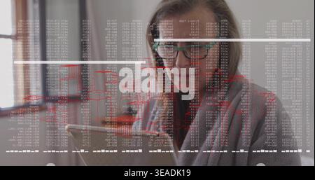 Working woman wearing gray sweater and green glasses focusing on laptop at desk, with code overlays Stock Photo