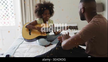 Playing girl strumming acoustic guitar on bed in bedroom while man clapping, star overlay Stock Photo
