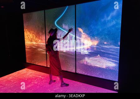 13 January 2026, Dubai Expo City, UAE: Woman touching a large screen showcasing colorful digital light art, creating an immersive futuristic experienc Stock Photo