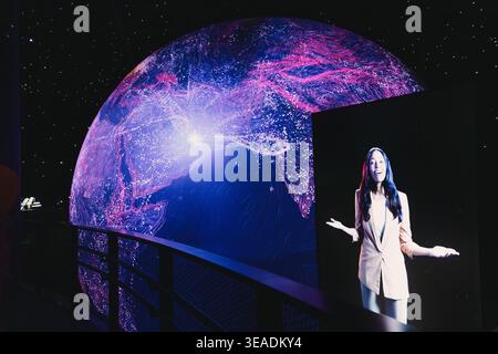 13 January 2026, Dubai Expo City, UAE: Woman presenting at an interactive digital exhibit with a large curved screen showing global data networks and Stock Photo