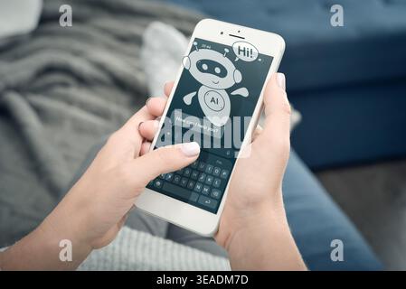 Close-up of woman hands holding smartphone at home. AI assistant chatbot on the screen with message “Hi!”. Concept of virtual support, artificial inte Stock Photo