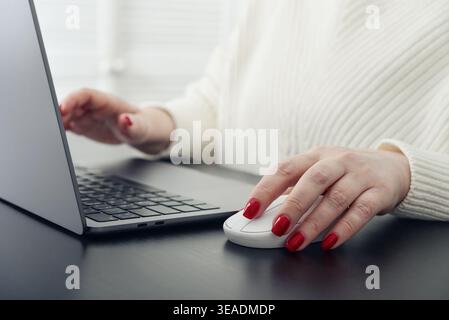 Close up of female hands with red manicure typing on a laptop keyboard. Concept of remote work, online communication, digital services, and modern lif Stock Photo