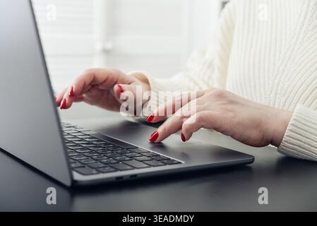 Close up of female hands with red manicure typing on a laptop keyboard. Concept of remote work, online communication, digital services, and modern lif Stock Photo