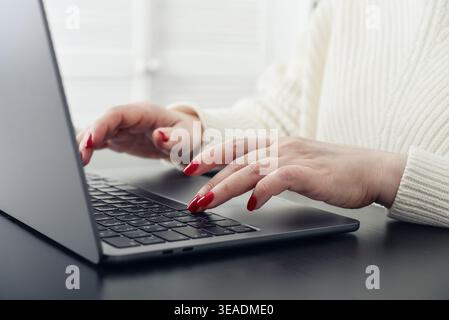 Close up of female hands with red manicure typing on a laptop keyboard. Concept of remote work, online communication, digital services, and modern lif Stock Photo