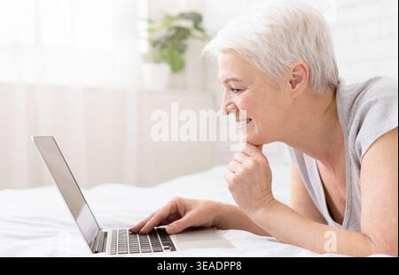Woman lying in bed and watching something on laptop Stock Photo