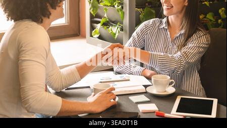 Young colleagues handshaking during informal meeting in cafe Stock Photo