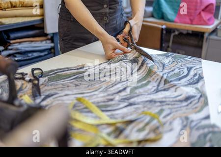 Cutting Fabric with Scissors on Worktable in Atelier Stock Photo