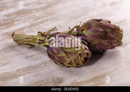 Two fresh raw globe artichokes displayed on textured light white wooden background. Healthy organic vegetable, still life food photography. Natural li Stock Photo