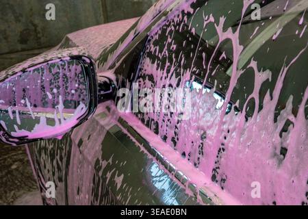 Car covered with pink foam at self service car wash station, close up side mirror detail. Concept: car cleaning process Stock Photo