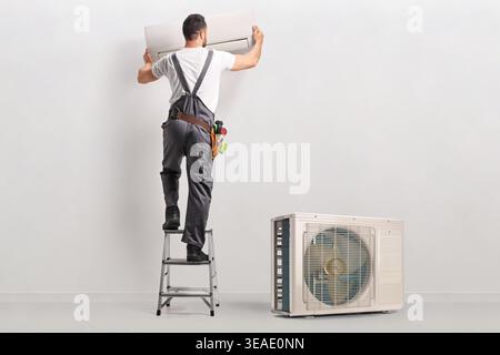 Technician on a ladder installing indoor air conditioning unit on a wall Stock Photo