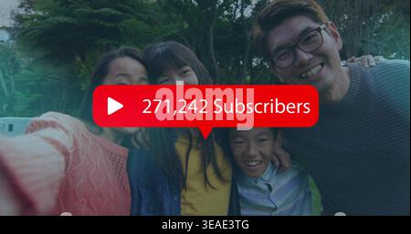 Smiling family posing selfie at park, woman in coral sweater holding phone showing 271k Subscribers Stock Photo