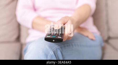 Senior woman using TV remote control on sofa at home Stock Photo