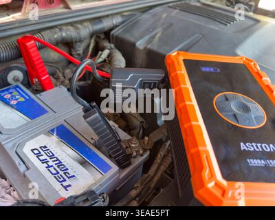 Astro AI 1500A portable jump starter connected to a Techno Power car battery with jumper cables in a vehicle engine bay Stock Photo