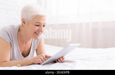 Happy senior woman lying in bed and using digital tablet Stock Photo