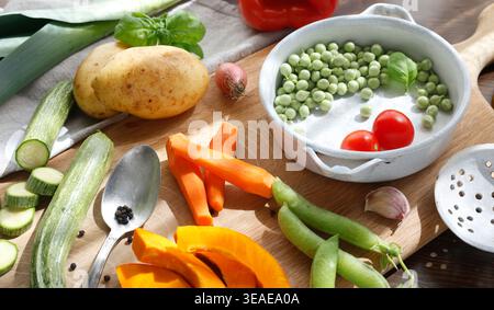 Assorted seasonal vegetables with vintage kitchen utensils on wooden cutting board. High-angle shot features sliced carrots pumpkin zucchini and Stock Photo