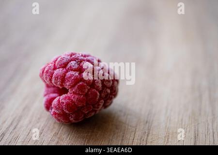 Close-up of a single frozen raspberry on a wooden surface with soft natural light and copy space. Stock Photo