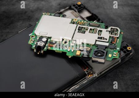 A technician is focused on repairing a smartphone that is disassembled on a work surface. Various parts are shown clearly. Stock Photo