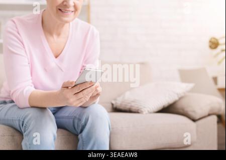 Cheerful aged woman using her smartphone at home Stock Photo